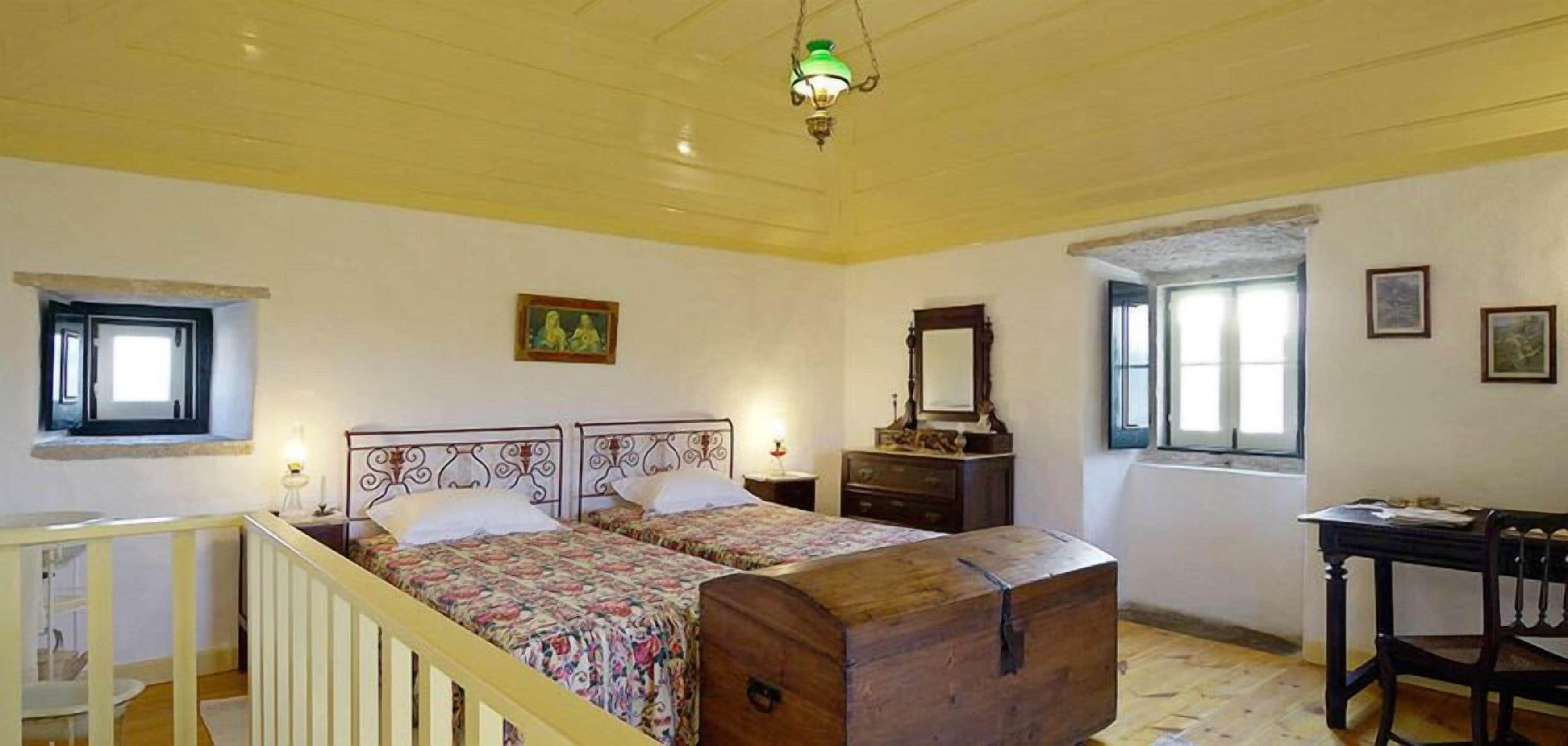 A room with two beds, a wooden chest, a dresser, a mirror, and a window.