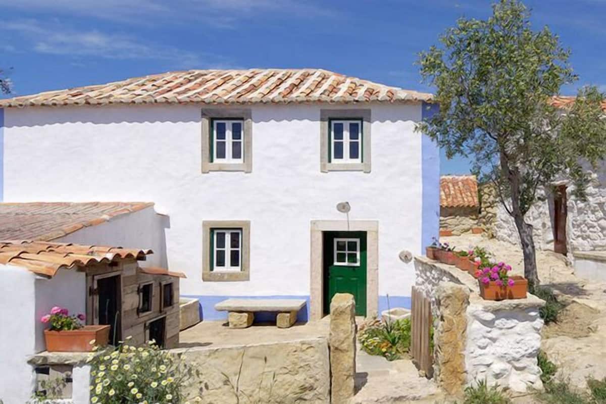 A traditional white building with a green door, a tiled roof, and stone walls.