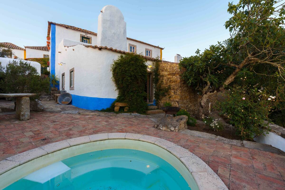 A pool area with a brick patio, a white building with blue trim, and a stone wall.