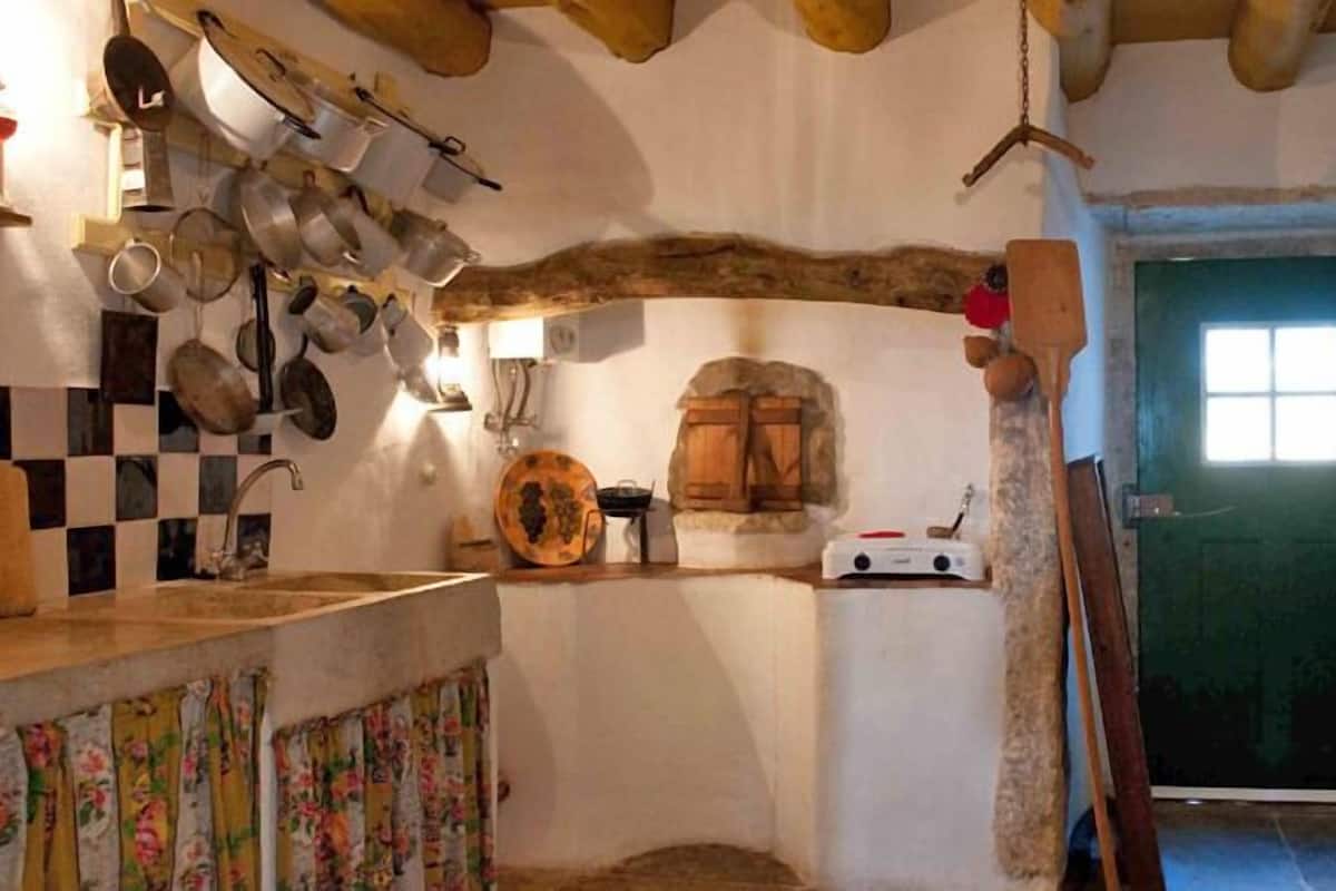 A rustic kitchen with a checkered backsplash, hanging pots, and a wooden door.
