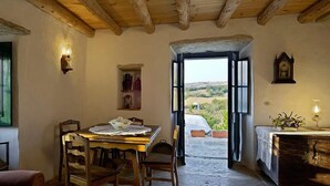 A rustic dining area with a wooden table and chairs, a view of the outdoors through a doorway, and a stone fireplace. - Aldeia da Mata Pequena (Mafra)