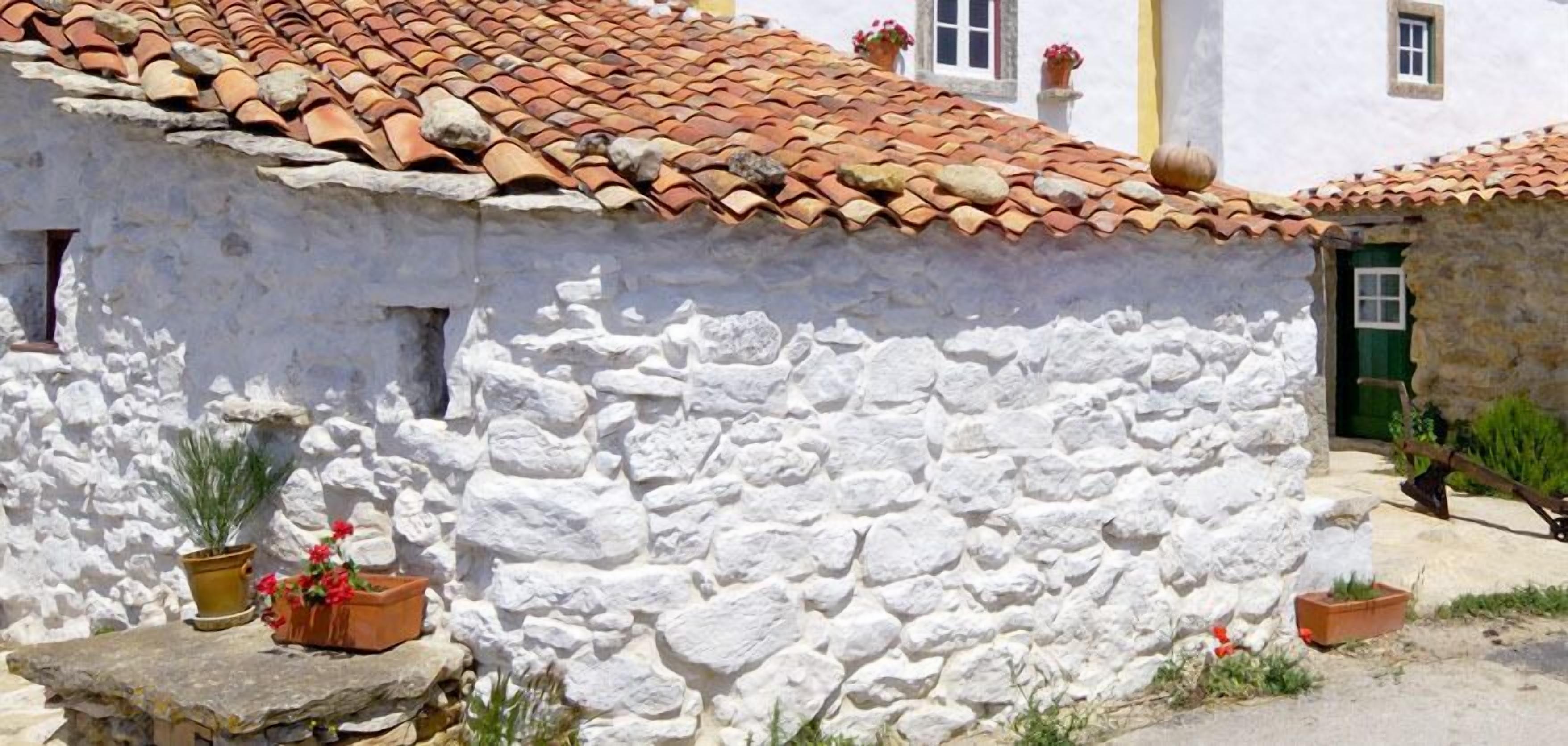 A traditional stone building with a tiled roof, white walls, and potted plants.