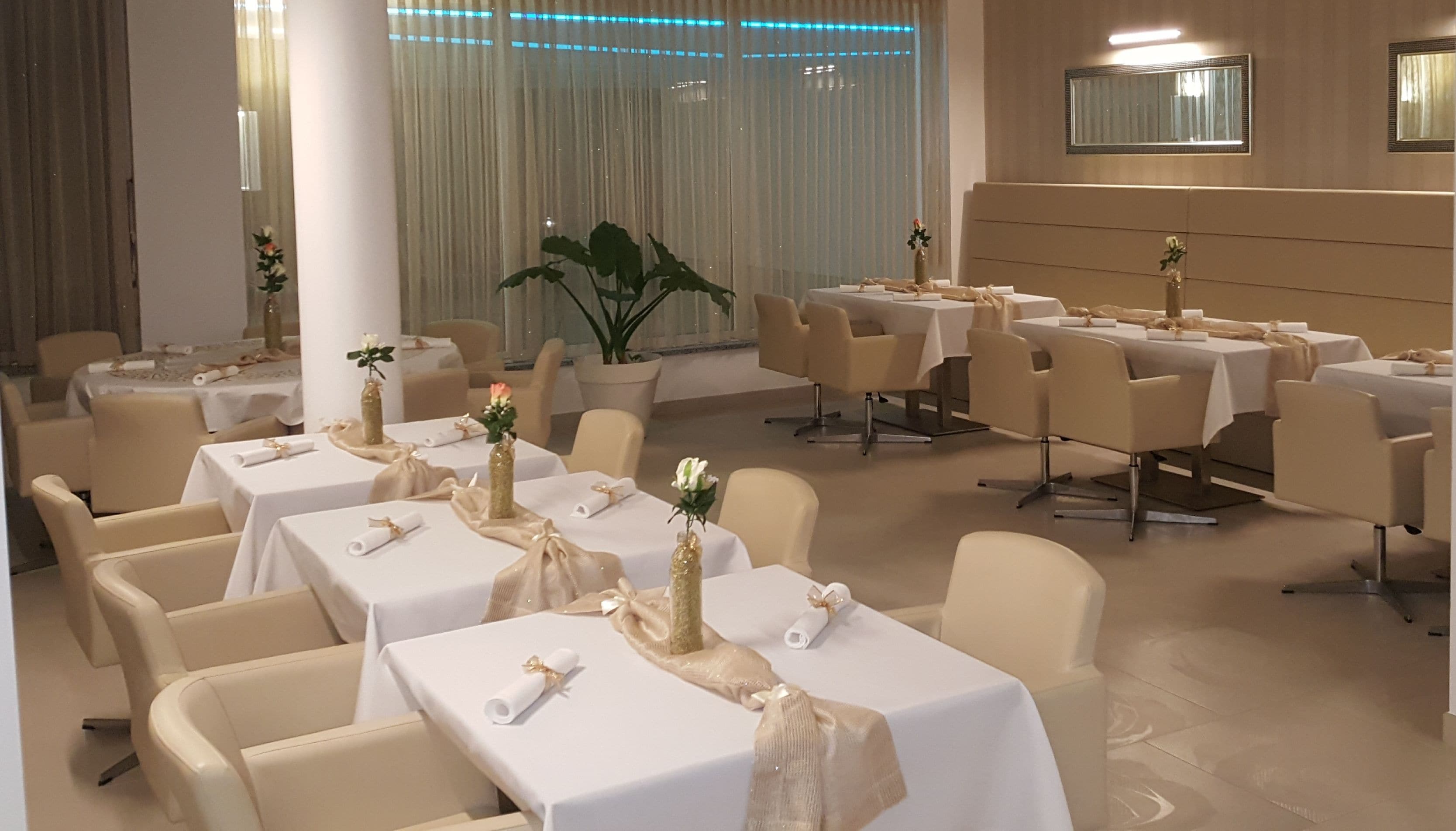 A banquet hall with round tables, white tablecloths, and gold sashes.