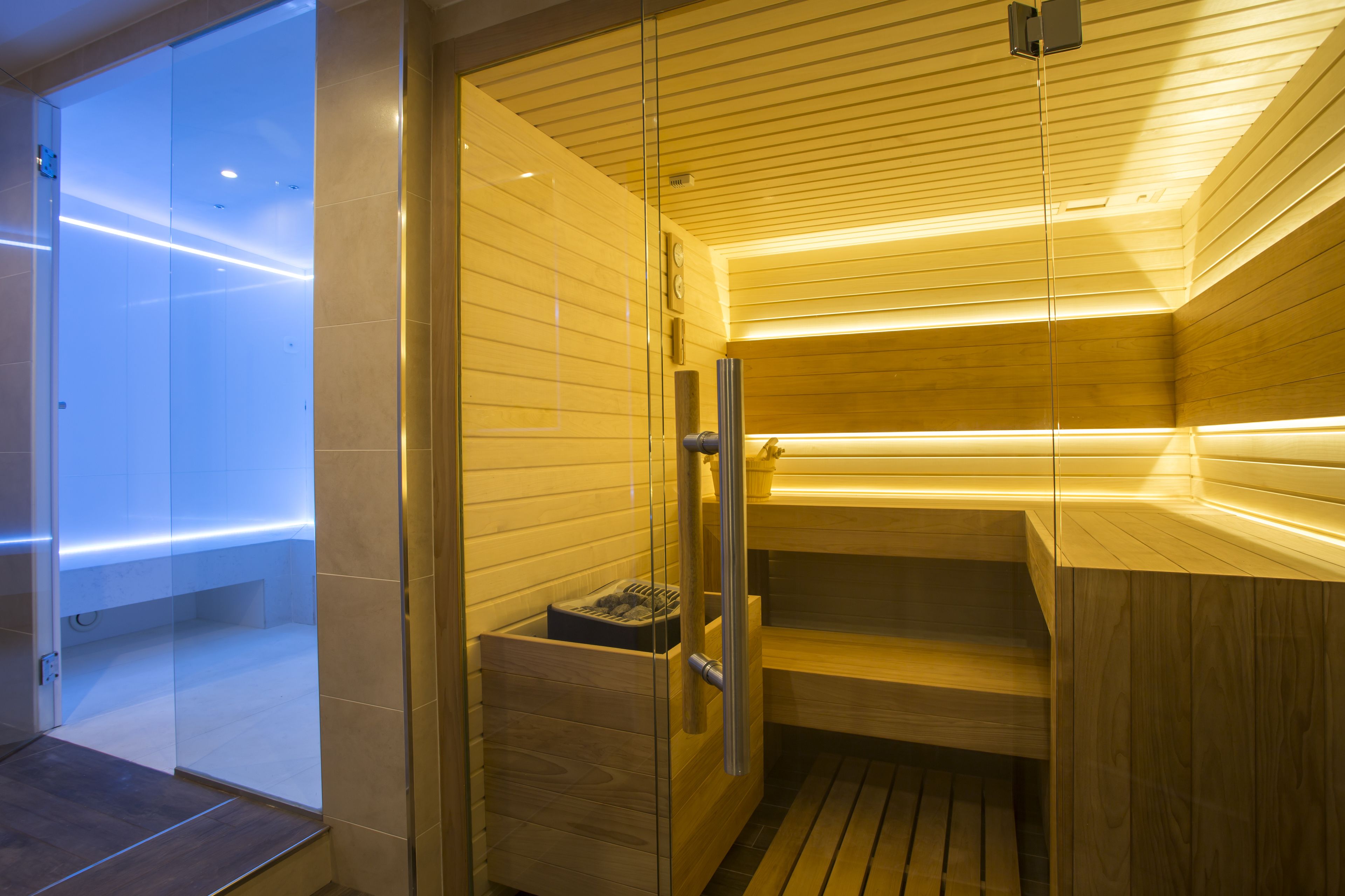 A modern sauna with wooden walls and a glass door, a wooden bench, and a bench with a towel.
