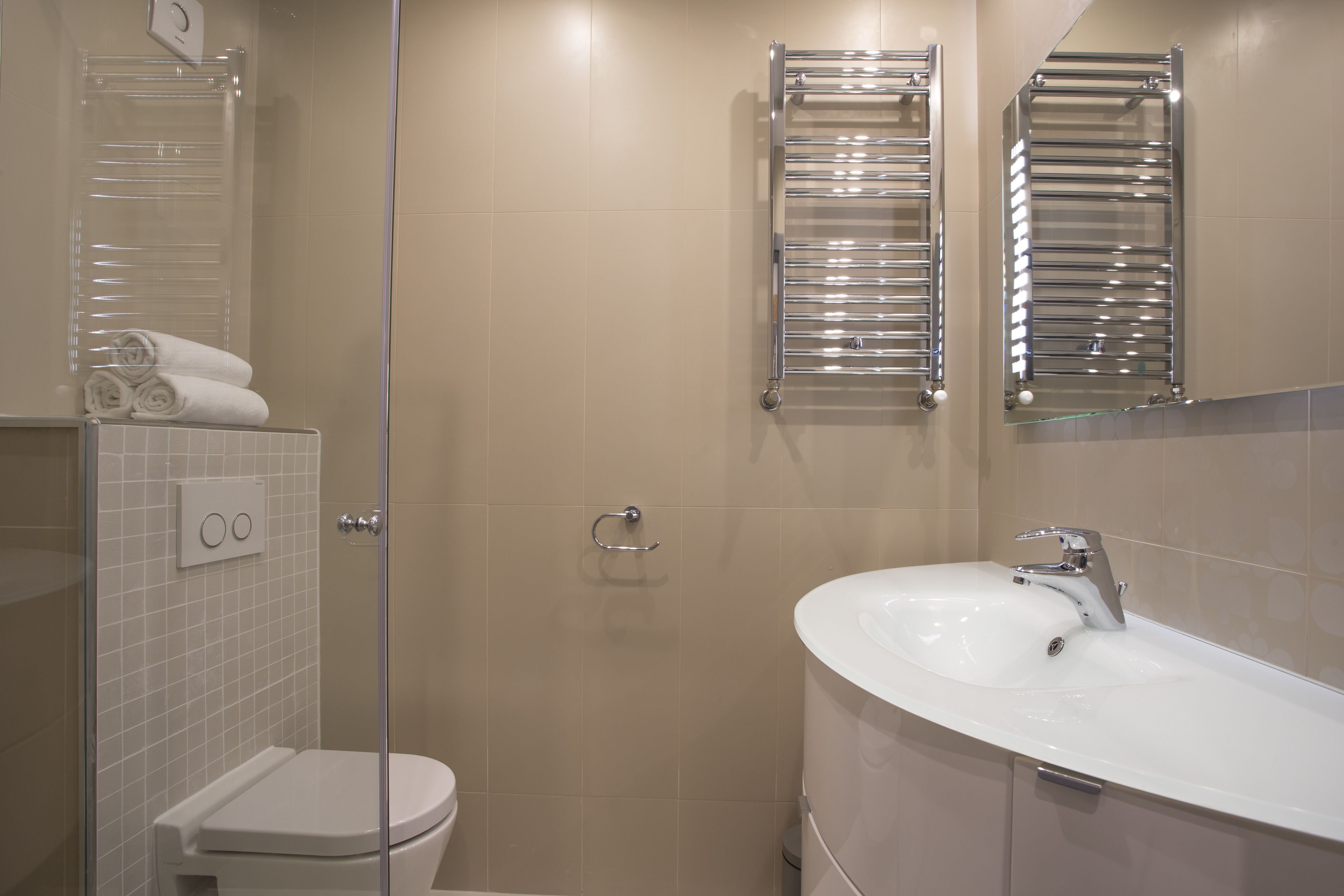A modern bathroom with a glass shower enclosure, a white toilet, a sink with a chrome faucet, and two towel racks.