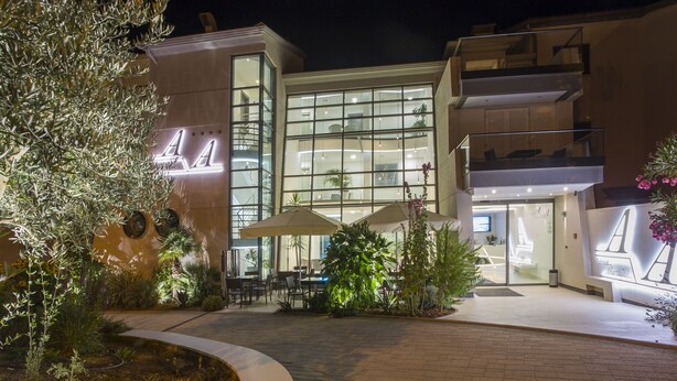 A modern hotel with a glass facade, outdoor seating area, and a well-lit entrance. - Adrion Aparthotel (Pula)