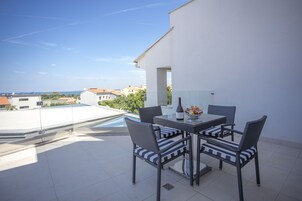 A terrace with a table and chairs, a pool, and a view of surrounding buildings.