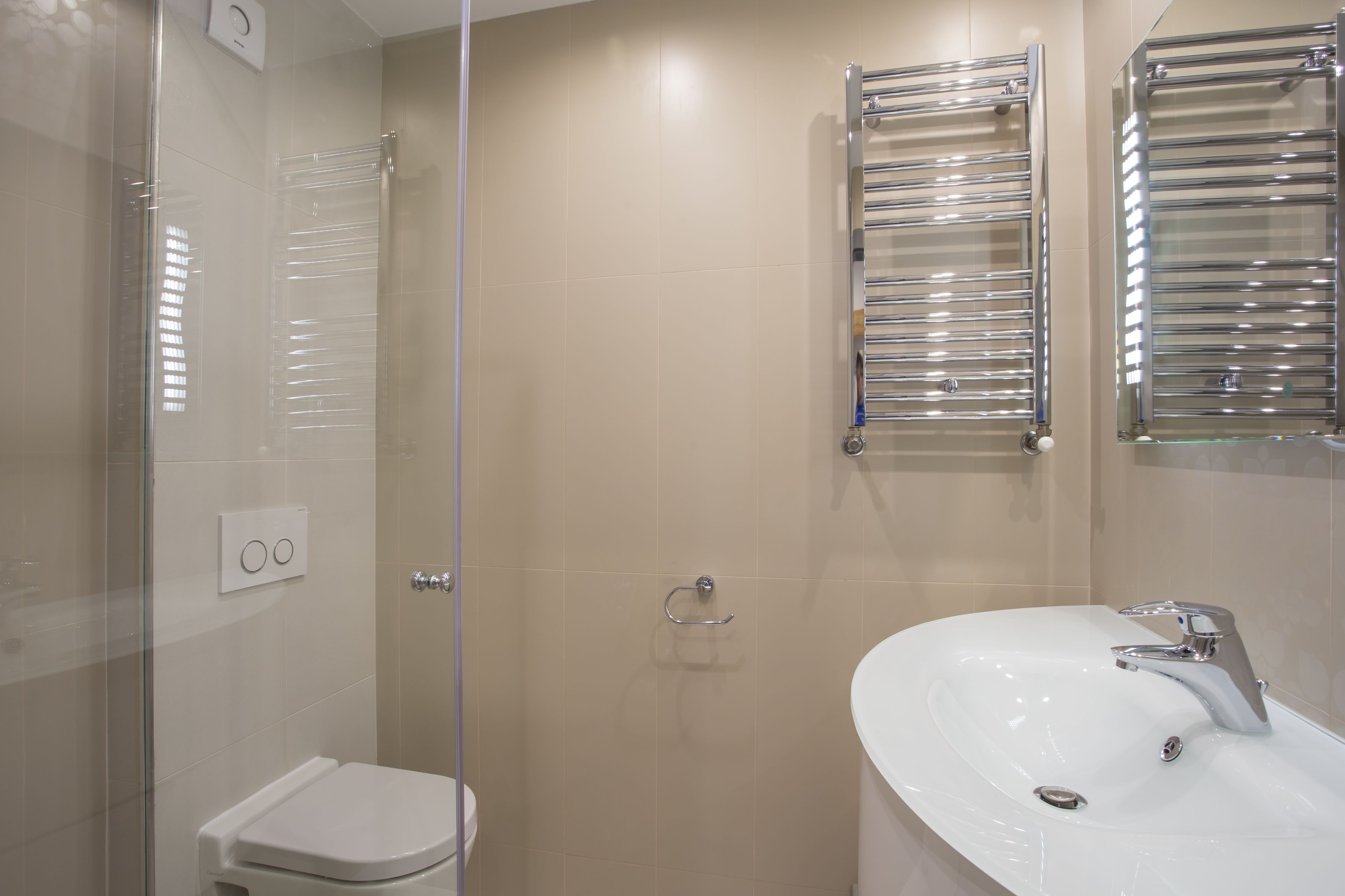 A modern bathroom with a glass shower enclosure, a white toilet, a glass-enclosed sink, and two chrome towel racks.