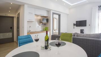 Un salón moderno con una mesa redonda blanca, dos sillas azules, un sofá gris y un televisor de pantalla plana montado en la pared.