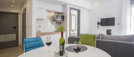 A modern living room with a white round table, two blue chairs, a grey sofa, and a flat-screen TV mounted on the wall.