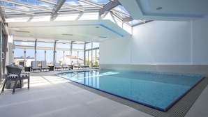 An indoor swimming pool with clear glass ceilings, lounge chairs, and a view of the outside. - Adrion Aparthotel (Pula)