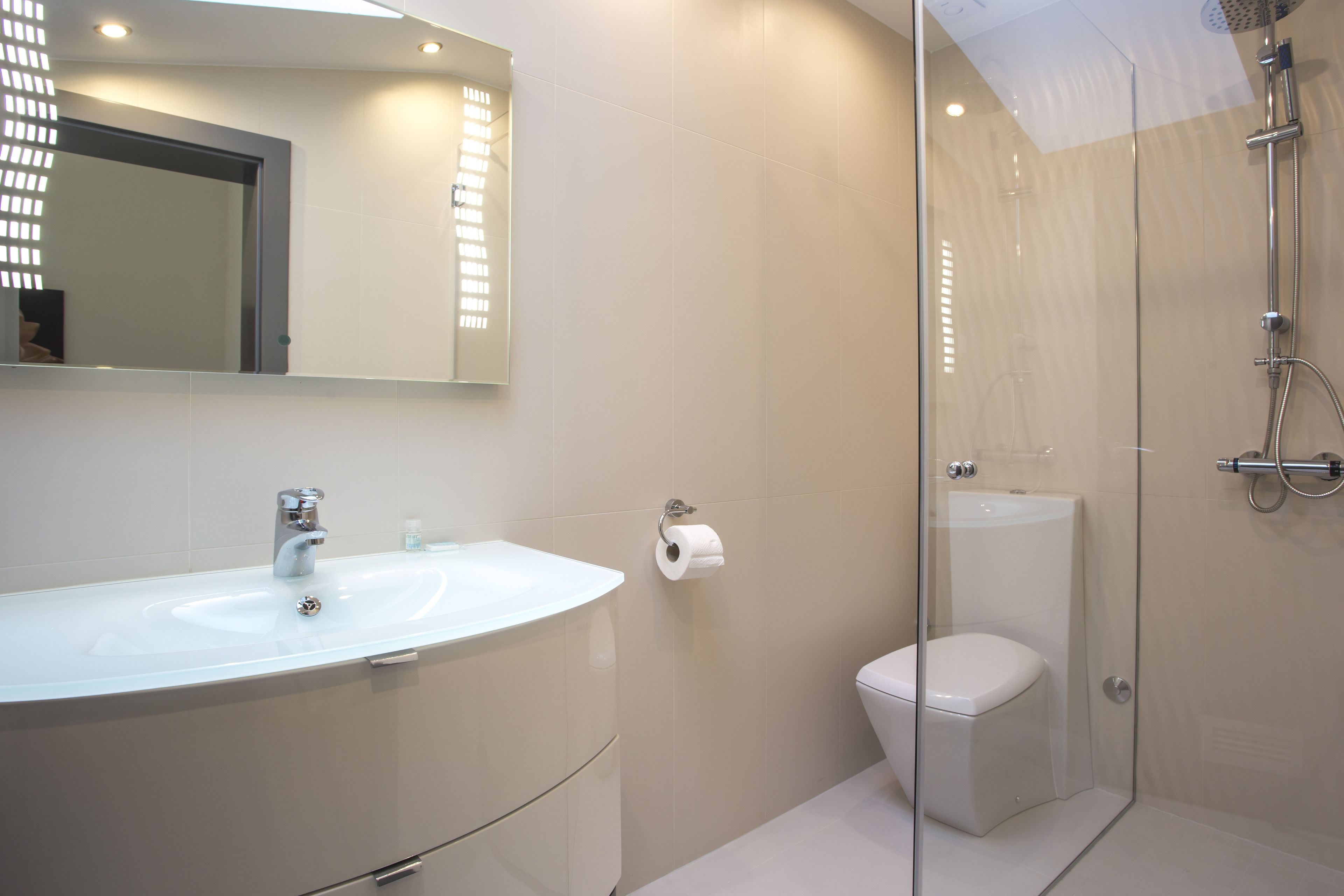 Un baño moderno con ducha de vidrio, lavamanos blanco y retrete.