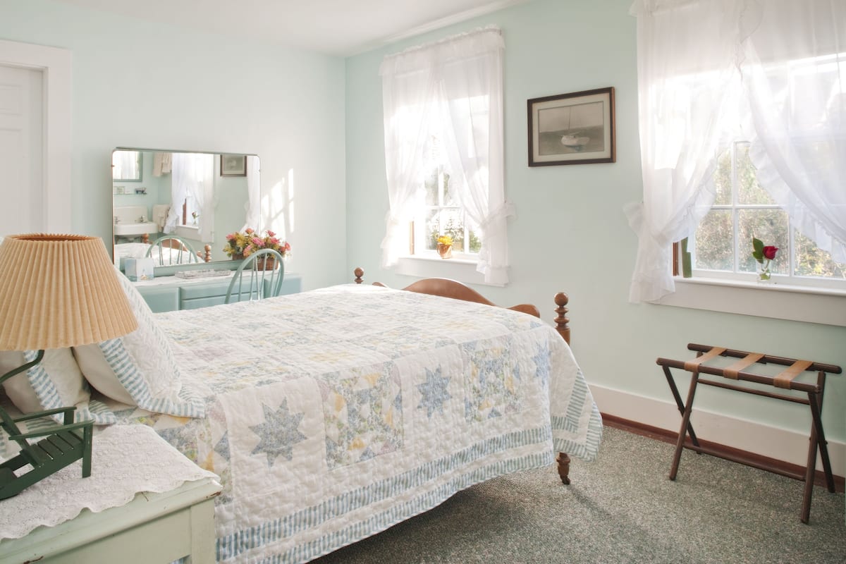 A bedroom with a bed, a chair, a small table, and a window with curtains.