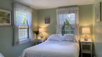 A bedroom with a bed, two bedside tables, a chair, and a window with curtains.