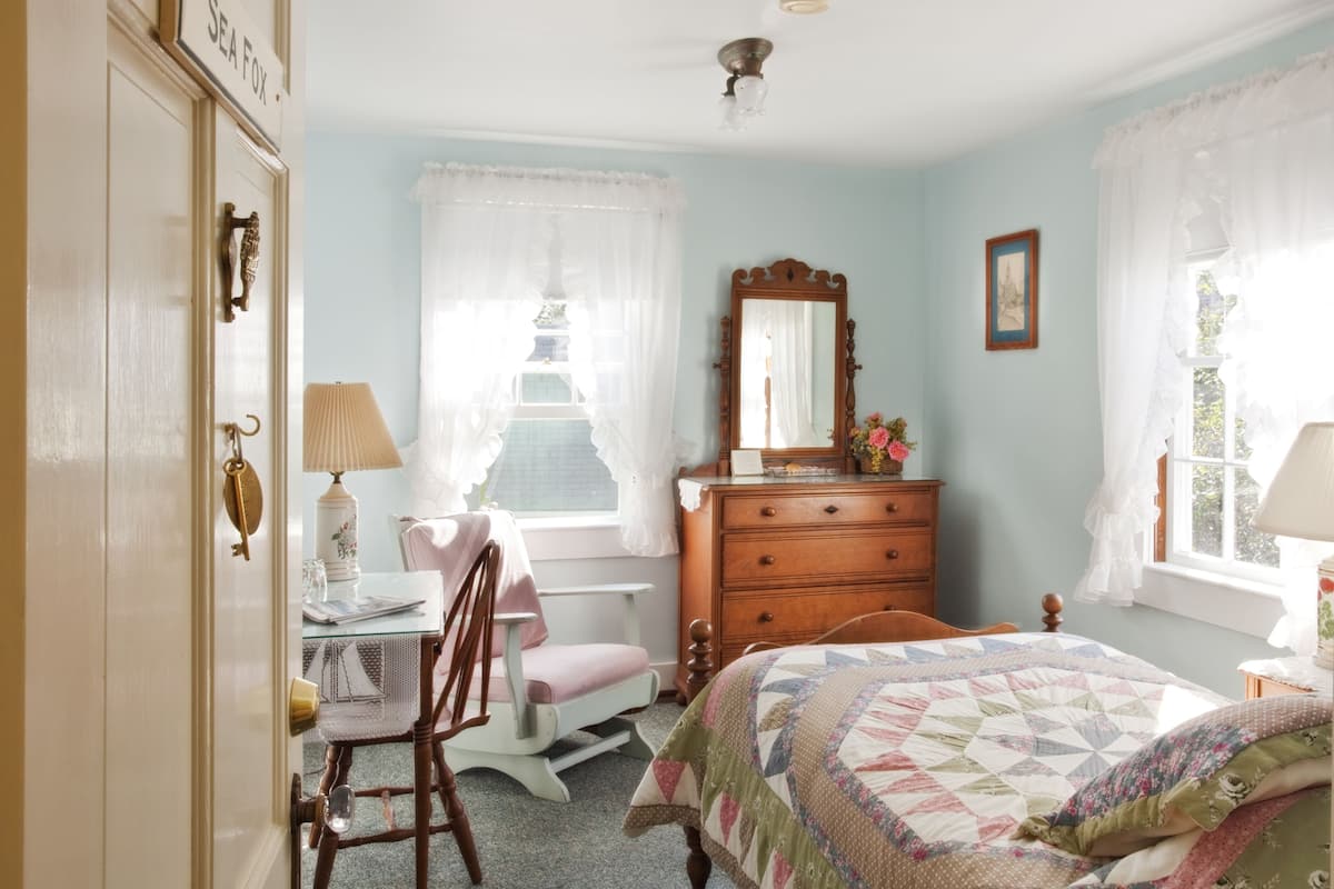 A bedroom with a bed, dresser, desk, chair, and a window with curtains.