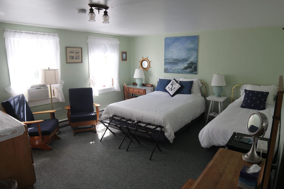 A bedroom with a bed, two bedside tables, a chair, a desk, and a window with curtains.