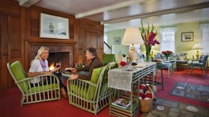 A cozy living room with green wicker chairs, a fireplace, and a dining area with a table set for two.