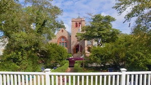 A church with a prominent tower and arched windows, surrounded by lush greenery and a white fence.