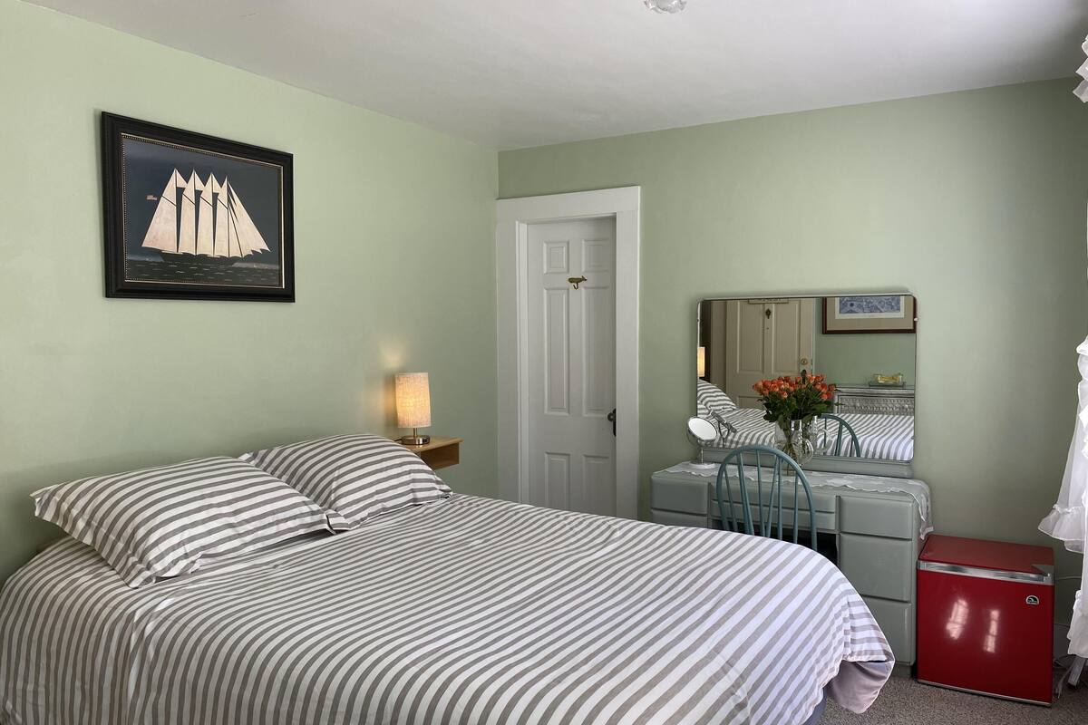 A bedroom with a bed, a nightstand, a dresser, a mirror, and a red appliance.