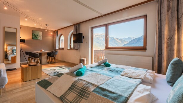 A modern hotel room with a large bed, a desk, and a television. - Alpin Resort Austria (Bichlbach)