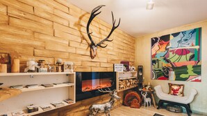 A cozy living room with a wooden wall, a fireplace, a deer sculpture, and a colorful painting. - Alpin Resort Austria (Bichlbach)