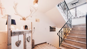 A wooden staircase with black railings, a wall-mounted deer antler, and a rustic wooden counter with heart-shaped decorations. - Alpin Resort Austria (Bichlbach)