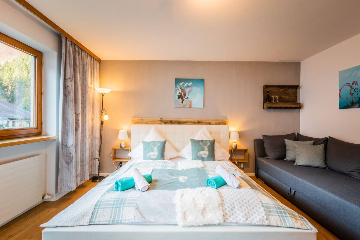 Un dormitorio con cama, sofá, ventana y obras de arte en las paredes.