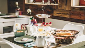 A breakfast table with a three-tiered serving tray, a bowl of cereal, a glass of orange juice, a basket of bread, and a small vase with a white flower. - Alpin Resort Austria (Bichlbach)