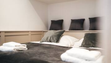 Una cama bien hecha con un cabecero oscuro, almohadas blancas y toallas blancas dobladas.