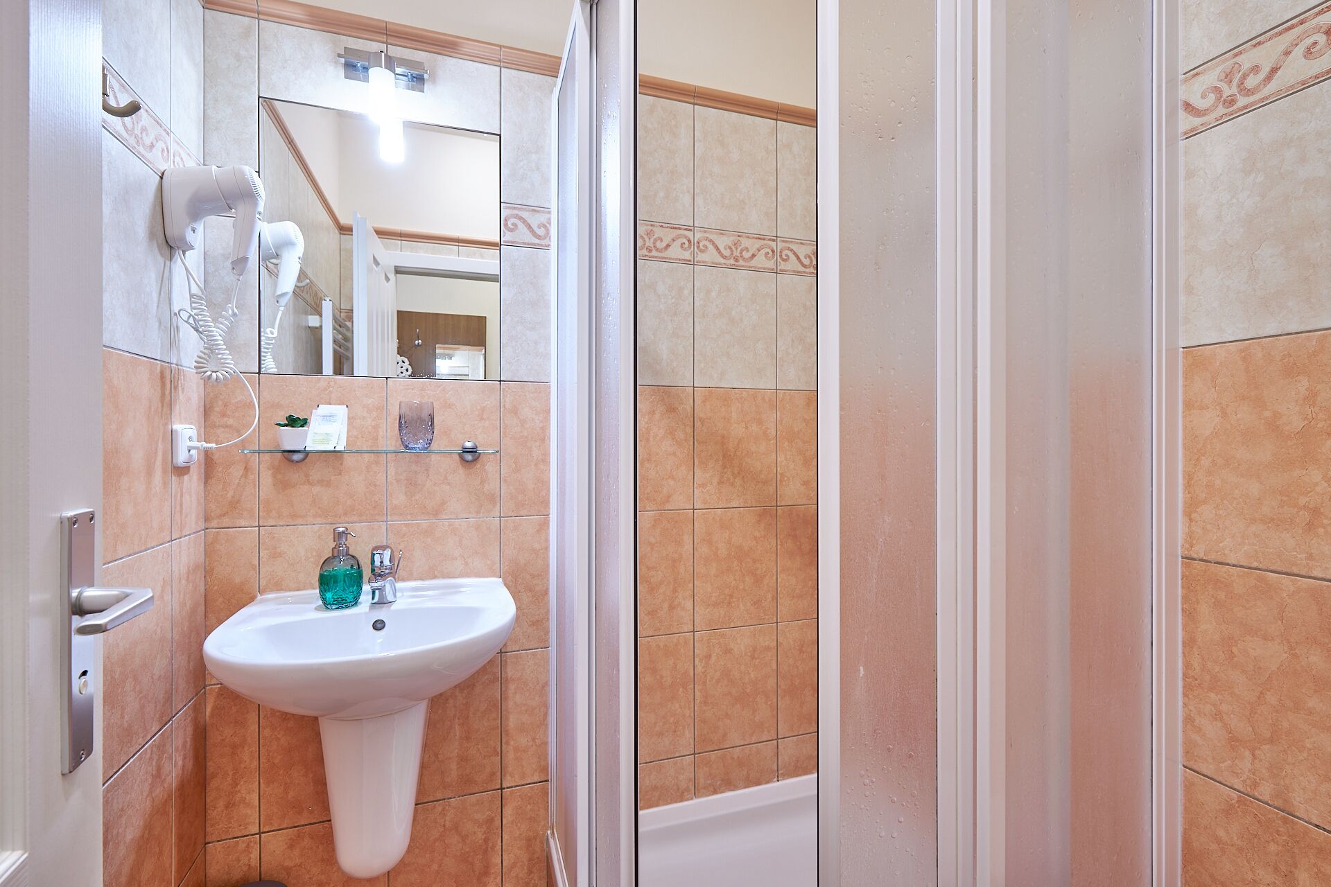Un baño con un lavamanos pedestal, un secador de pelo, un vaso y un espejo.