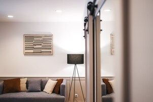 Una sala de estar moderna con un sofá gris, una lámpara de pie y una obra de arte minimalista en la pared.