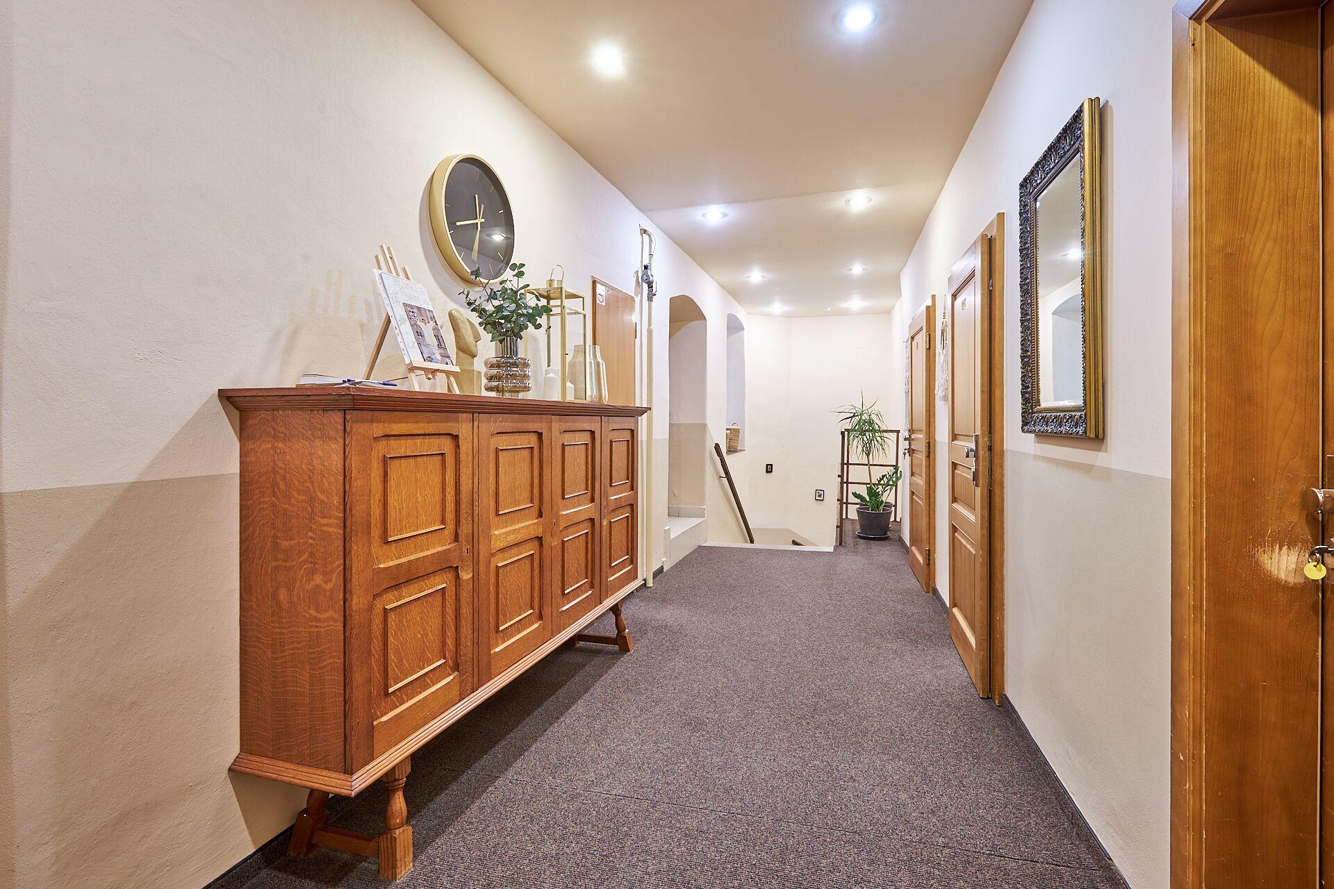 A hallway with a wooden cabinet, a round wall clock, and framed mirrors on the walls.
