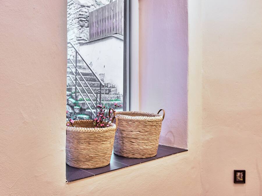 Una ventana con dos cestas tejidas sobre un alféizar negro, con vista a una escalera de piedra y un edificio.