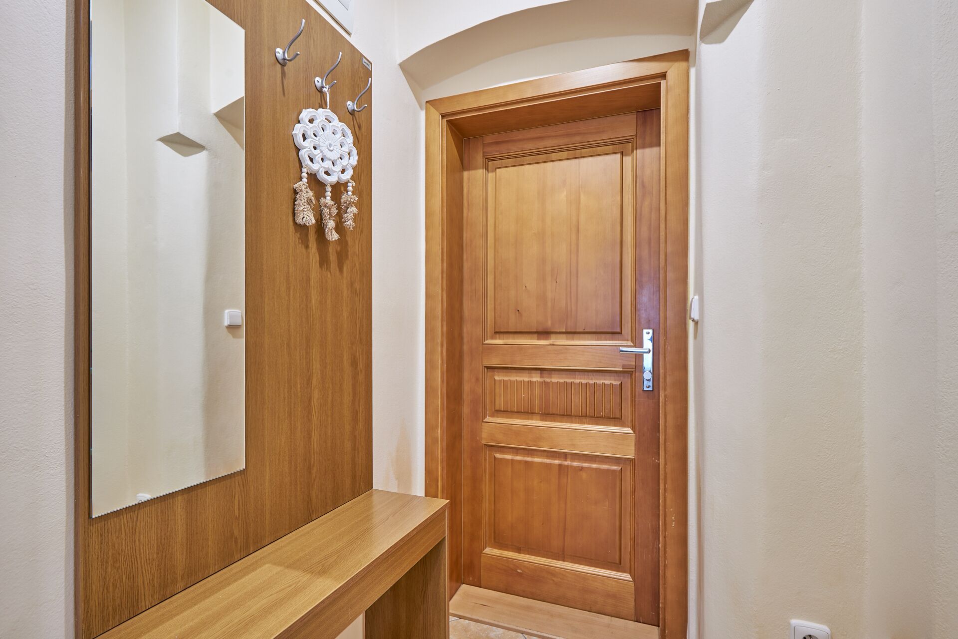 Una puerta de madera con un picaporte y una cerradura, un espejo encima y un banco de madera en el pasillo.