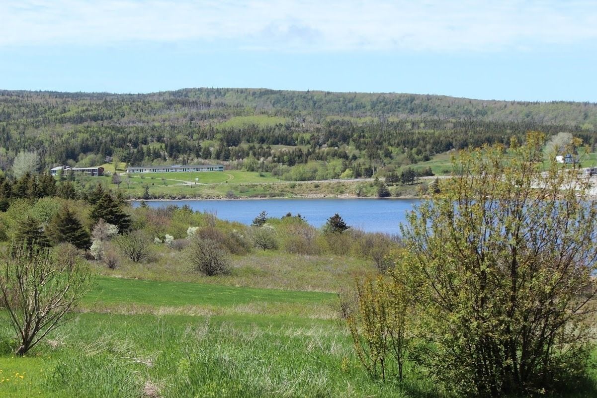 Vista de un lago con un edificio al fondo, rodeado de vegetación y colinas.