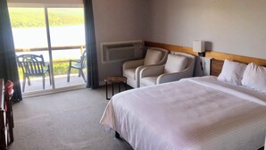 A hotel room with a bed, a seating area with chairs, a small table, and a view of the outdoors. - Duck Cove Inn (Margaree Harbour)