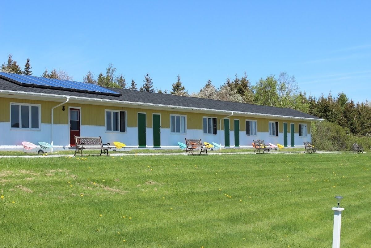 Un edificio giallo con tetto solare, un prato verde e diverse zone relax all'aperto con panche.