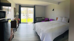 A hotel room with a bed, a desk, a chair, a television, and a sliding glass door leading to a balcony. - Duck Cove Inn (Margaree Harbour)
