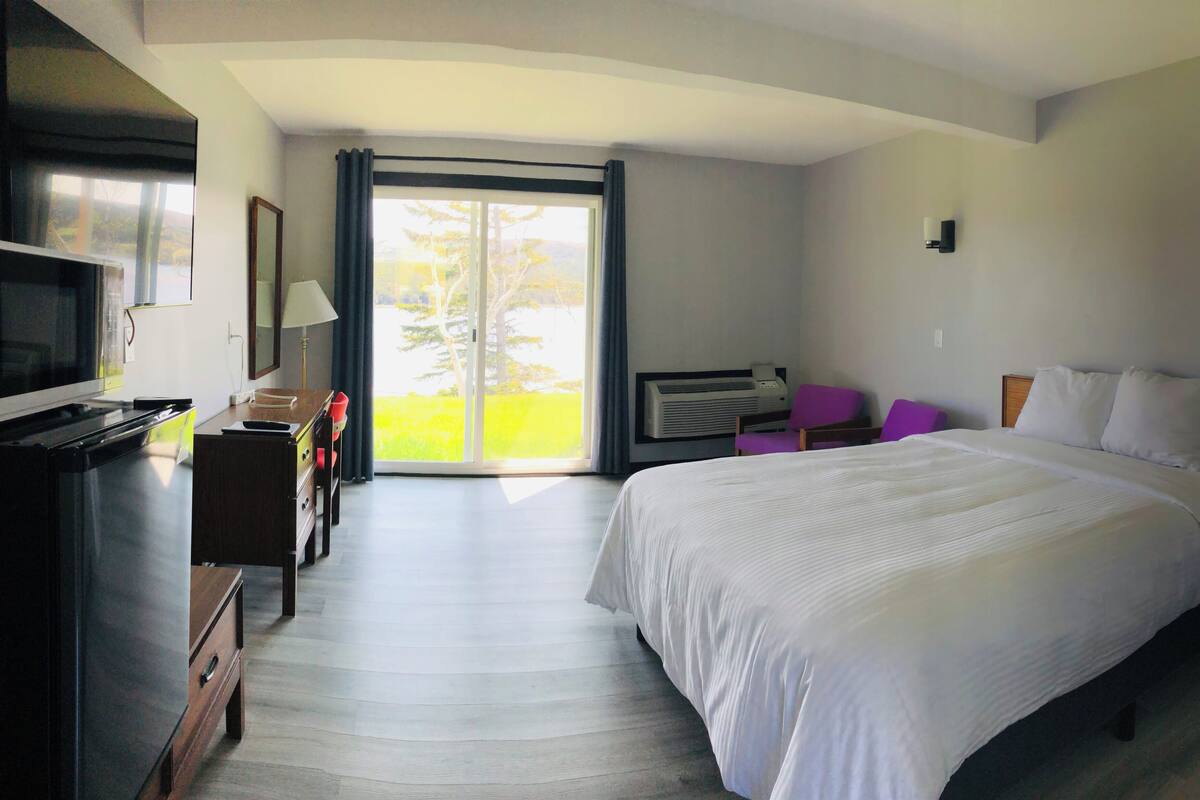 A hotel room with a bed, a desk, a chair, a television, and a sliding glass door leading to a balcony.