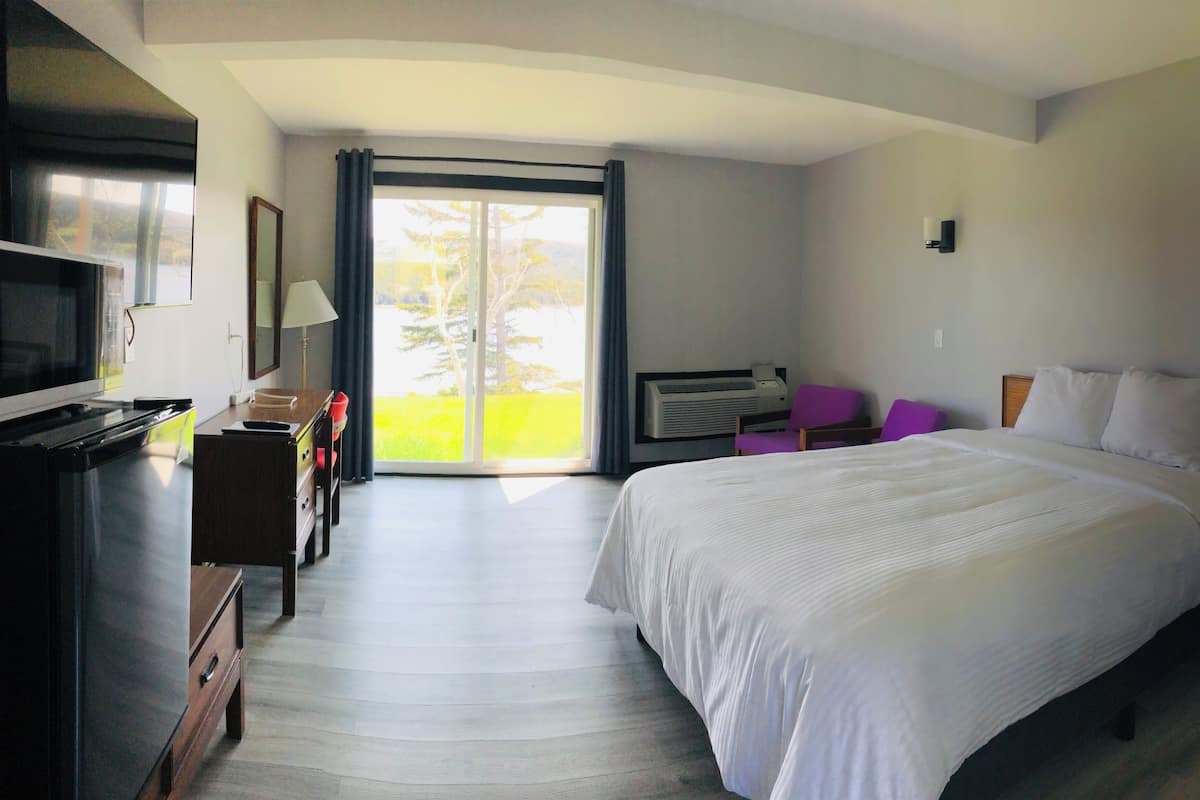 A hotel room with a bed, a desk, a chair, a television, and a sliding glass door leading to a balcony.