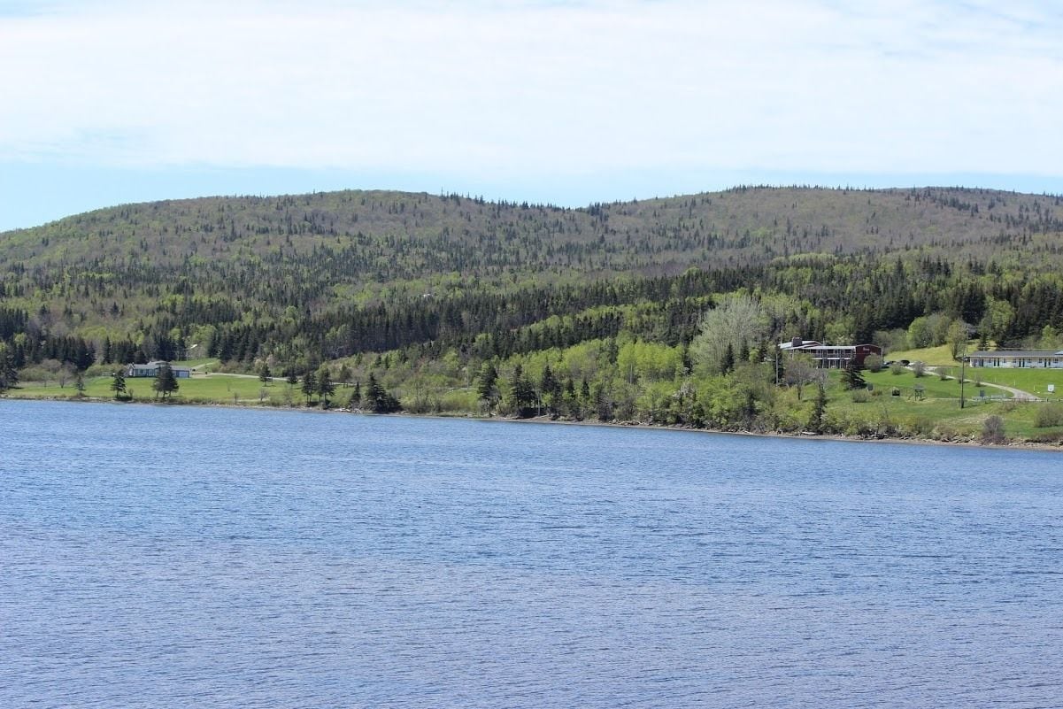 A lakeside view with a forested hill in the background and a building with a dock.
