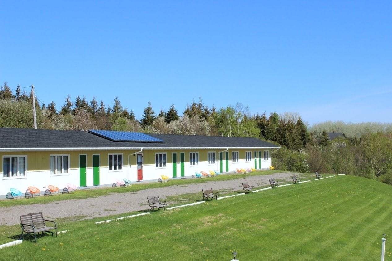 A row of single-story buildings with a green door, a solar panel on the roof, and a grassy area with benches.