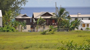 A coastal house with a balcony, surrounded by lush greenery and a view of the ocean. - Sea View Apartment (Silver Sands)
