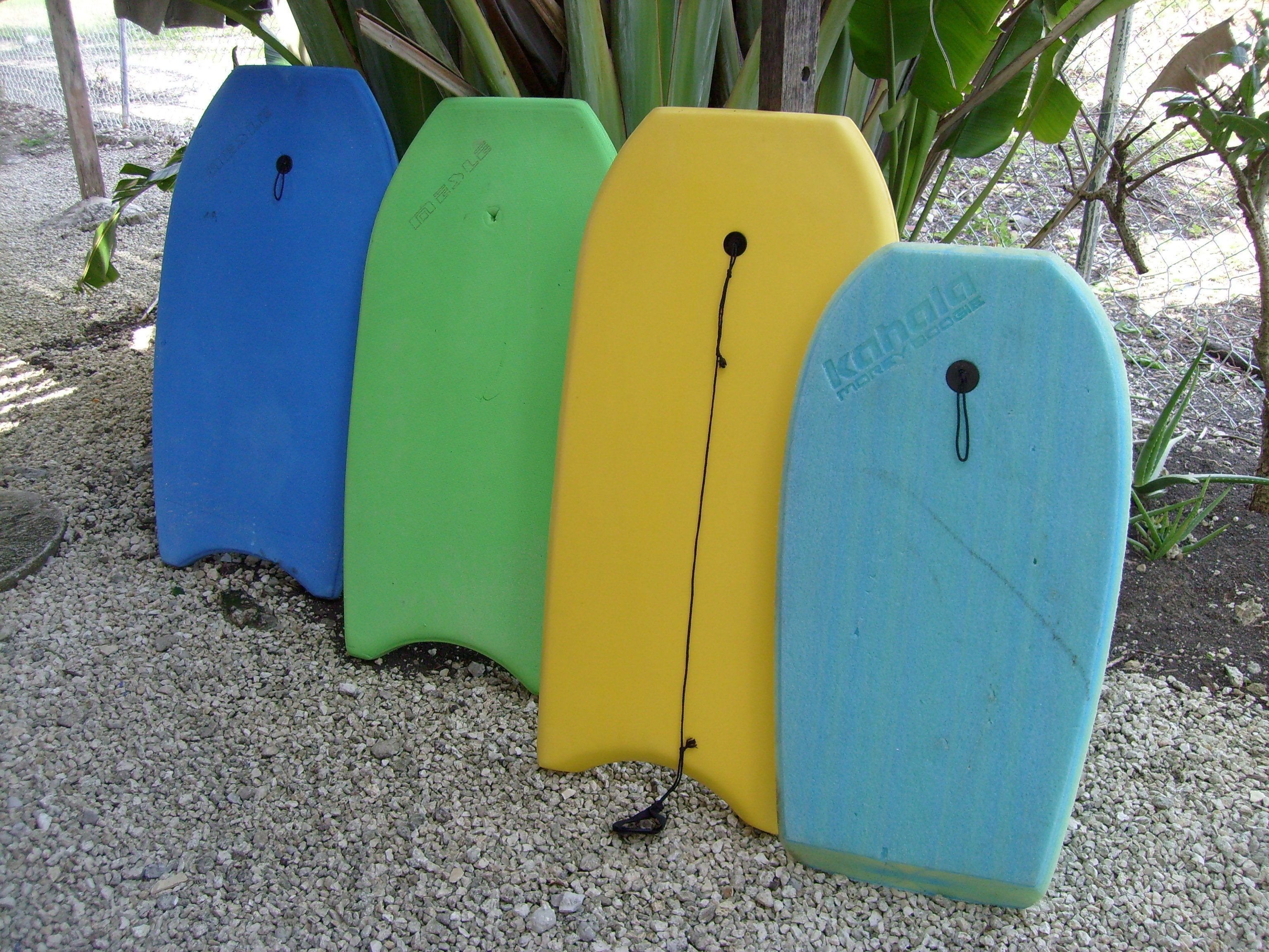 Four surfboards of different colors placed on gravel.