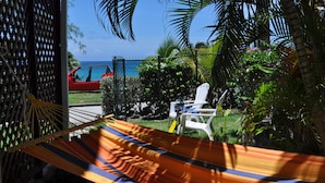A hammock in a shaded area with a view of the ocean and a red car parked nearby. - Sea View Apartment (Silver Sands)