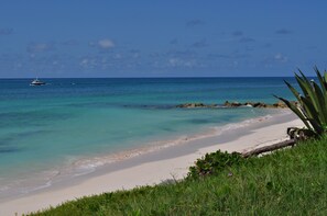A beach with clear turquoise water, a boat in the distance, and a rocky outcrop with vegetation. - Sea View Apartment (Silver Sands)