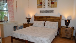 A bedroom with a wooden bed, two bedside tables with lamps, a nightstand, a dresser, and a window with a curtain. - Sea View Apartment (Silver Sands)