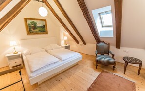 Ein Schlafzimmer mit Hochbett, gestreiftem Sessel, kleinem Tisch, einem Gemälde und einem Oberlicht.