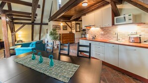Una cocina acogedora con vigas de madera a la vista, una zona de comedor con mesa y sillas, y una isla de cocina con fregadero y electrodomésticos.