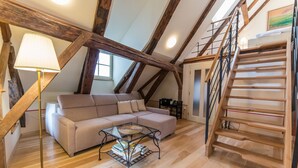 Una habitación estilo loft con vigas de madera a la vista, un sofá, una mesa de centro con libros, una lámpara y una escalera de madera.
